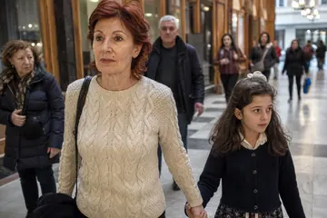 Yaşlı bir kadın kalabalık bir alışveriş pasajında torununun elini tutarak sakin ve kendinden emin adımlarla yürüyor